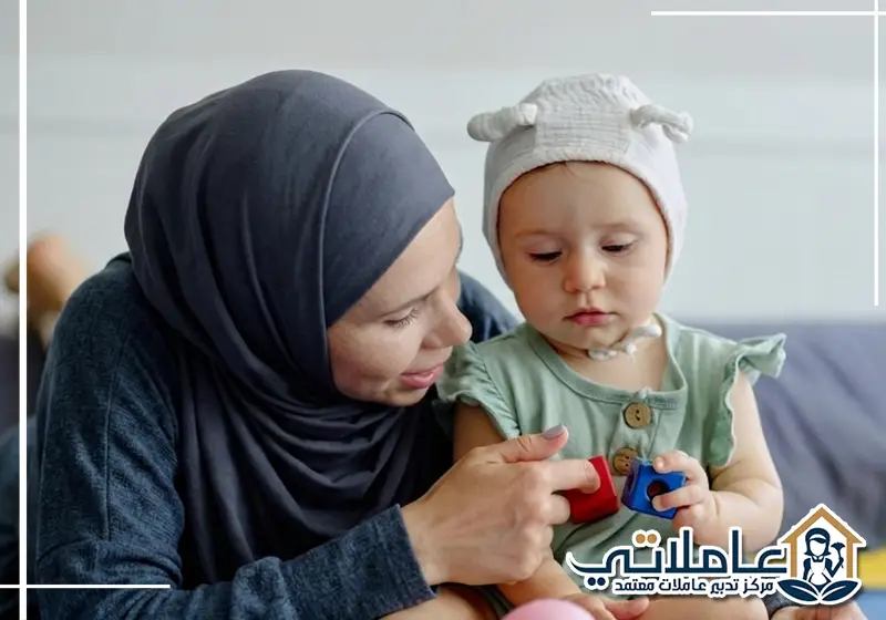 مربية أطفال تشارك طفلًا صغيرًا اللعب بالمكعبات داخل المنزل