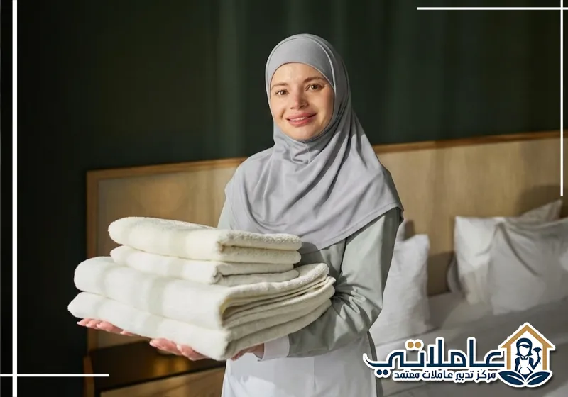 عاملة منزلية تحمل مناشف نظيفة ومرتبة ضمن خدمات خادمات بالشهر من مركز تدبير عاملاتي في الإمارات.